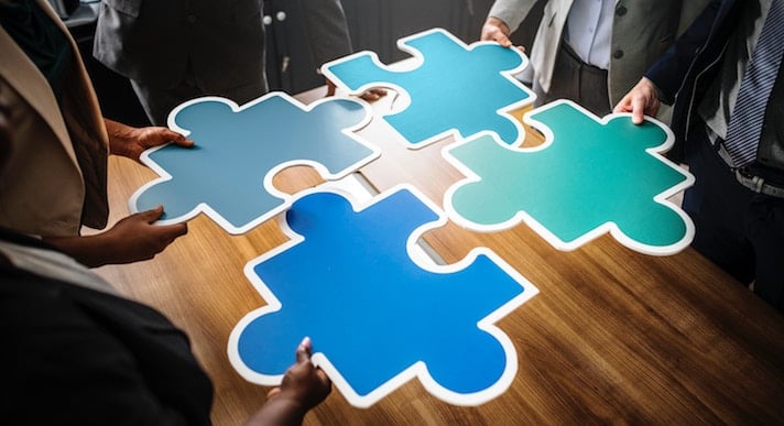 Four paper giant jigsaw pieces being held together by four people
