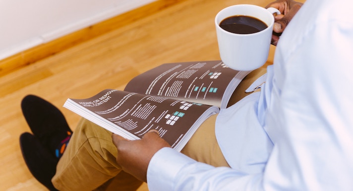 Man sat drinking coffee and reading a booklet